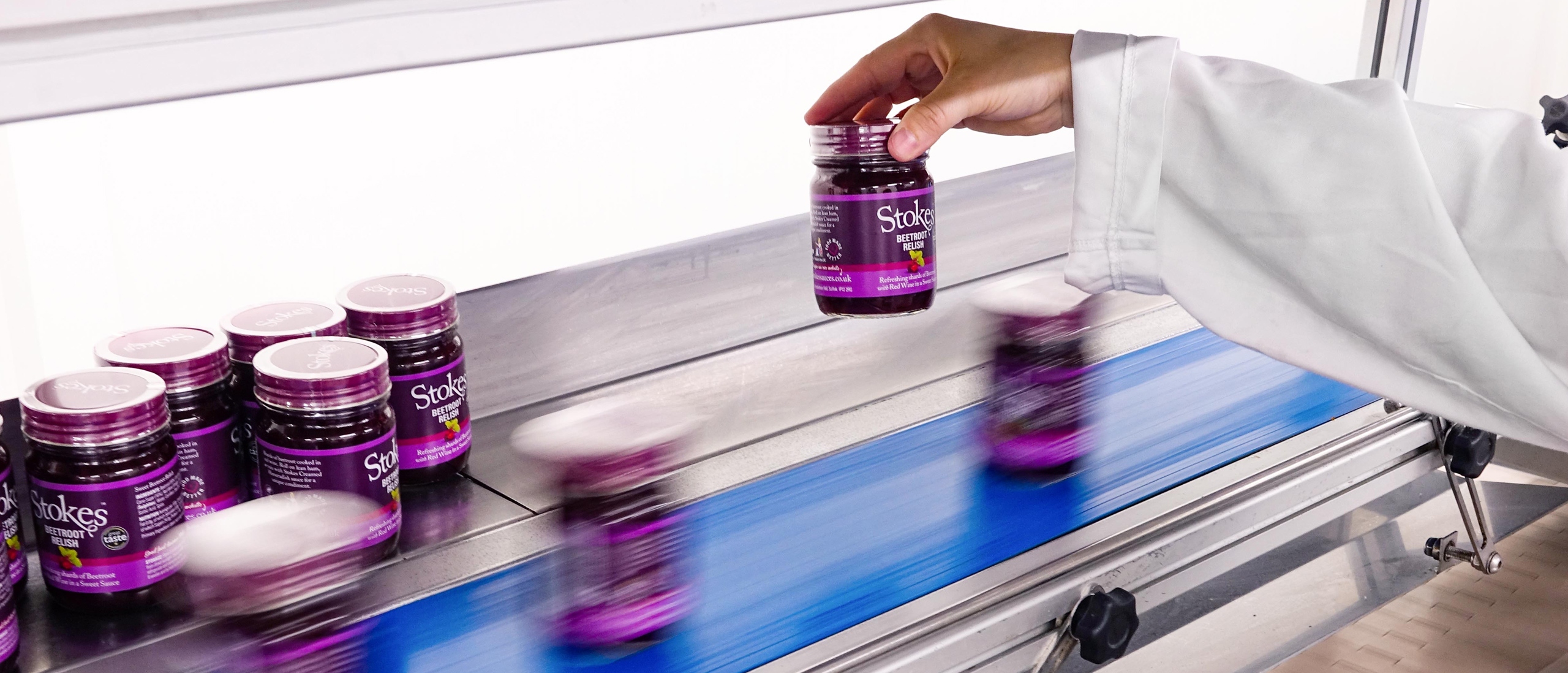 A hand picking a Stokes jar off of a production line.