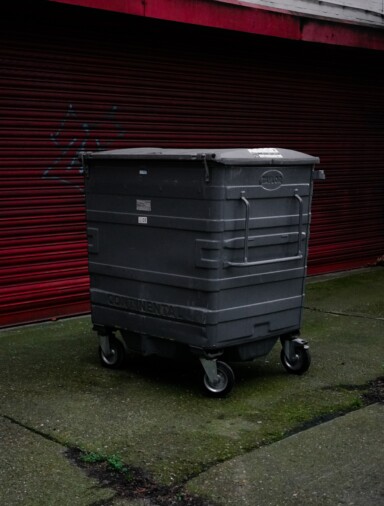 Grey industrial bin against a red wall