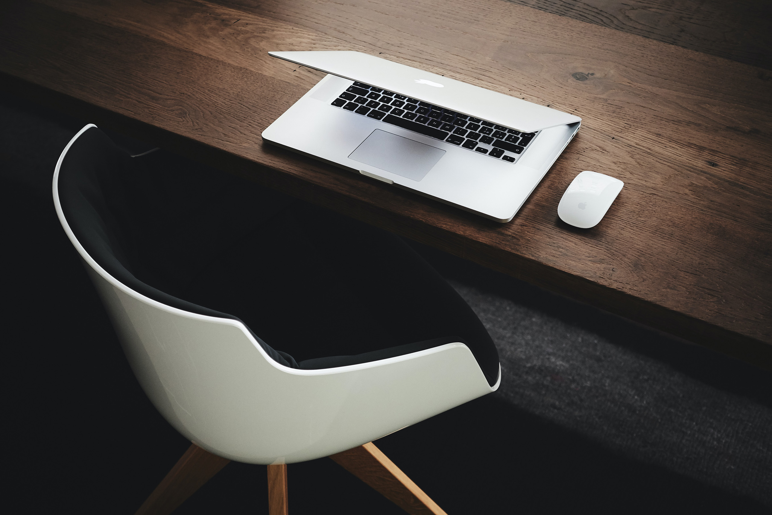 A chair at a desk that has a laptop and a mouse on it.