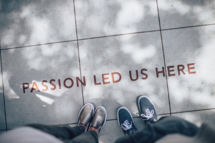 View looking down on two pairs of feet standing on tile with the text "PASSION LED US HERE"
