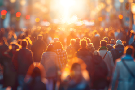 Blurred crowd of people walking on busy street, with sun setting in background